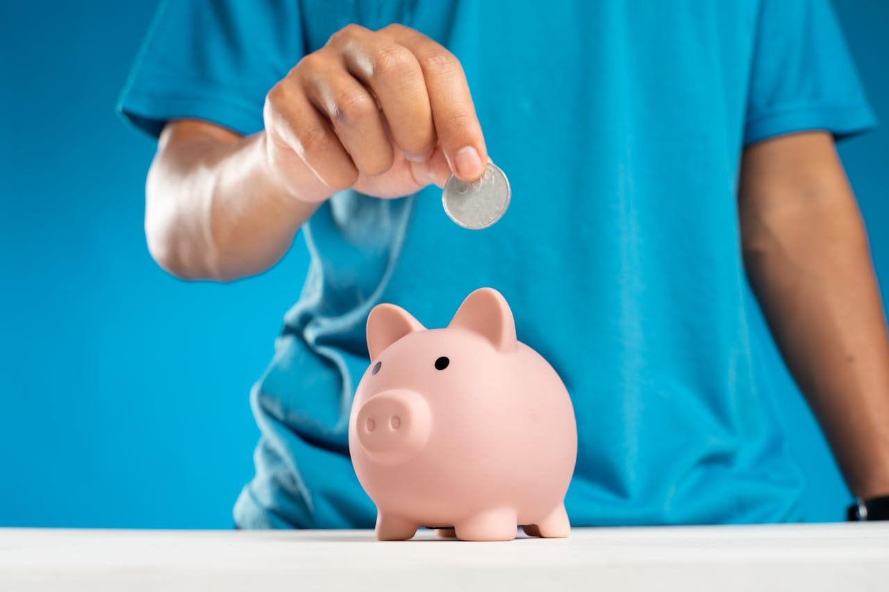 A close-up of an adults hand dropping a coin into a piggy bank, symbolizing savings and investment.